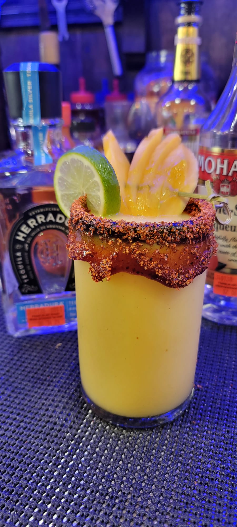 Creamy mango margarita with a thick chamoy chili rim, mango fan and lime wheel at the bar