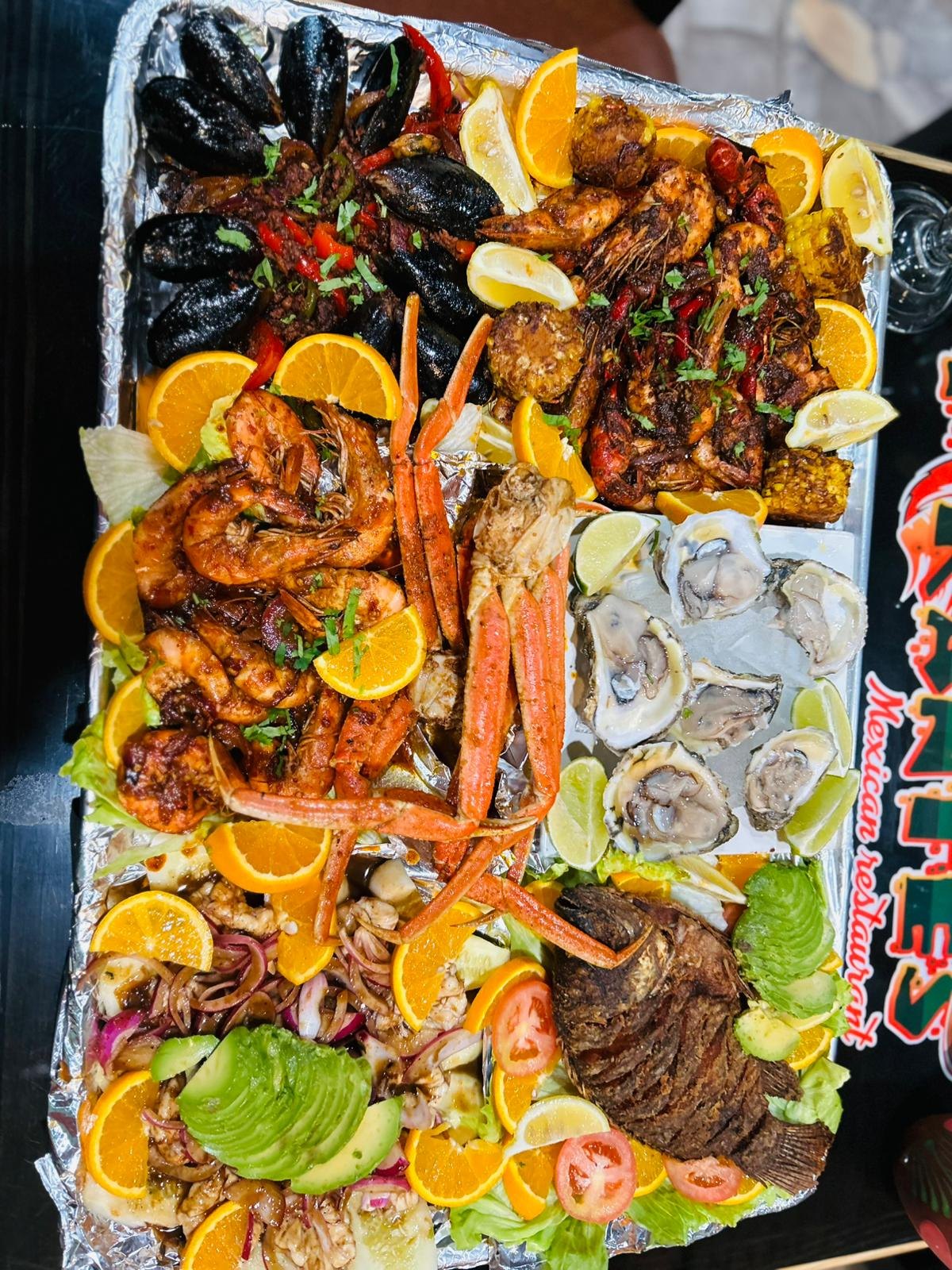 Overhead view of a large seafood tray with mussels, shrimp, crab legs, raw oysters, ceviche and fried tilapia