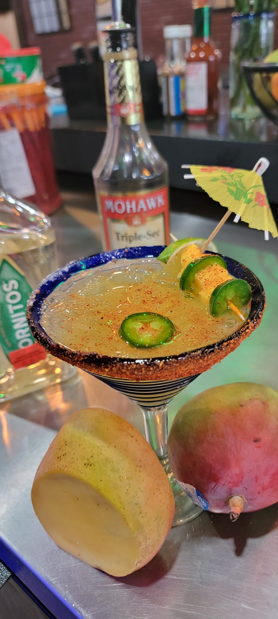 Mango jalapeño margarita in a blue-rimmed glass with chili salt, jalapeño slices and a paper umbrella