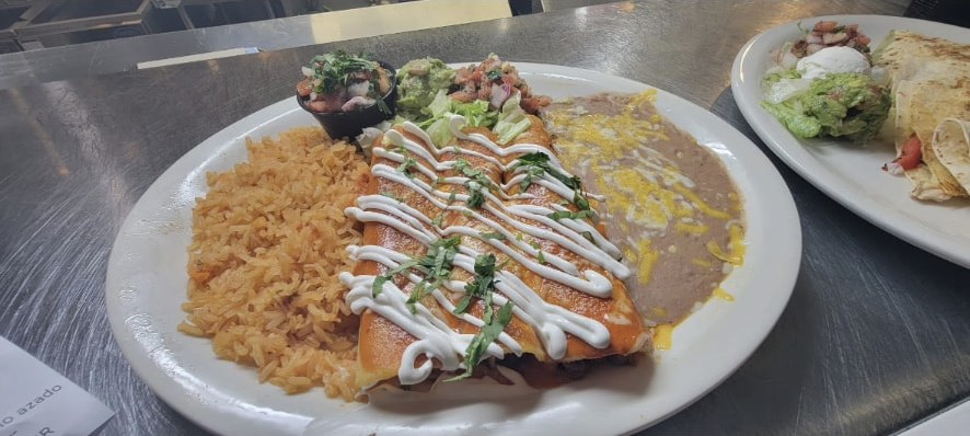 Enchiladas topped with crema, served with Mexican rice, refried beans and guacamole