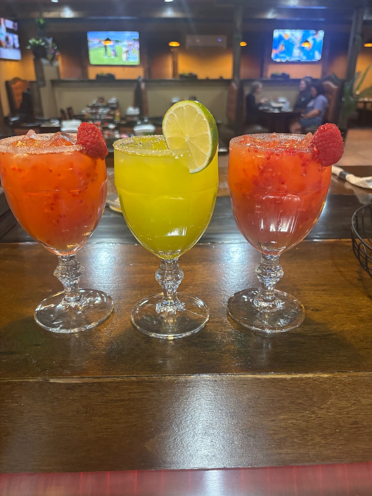 Three fruit margaritas with sugared rims garnished with raspberry and lime