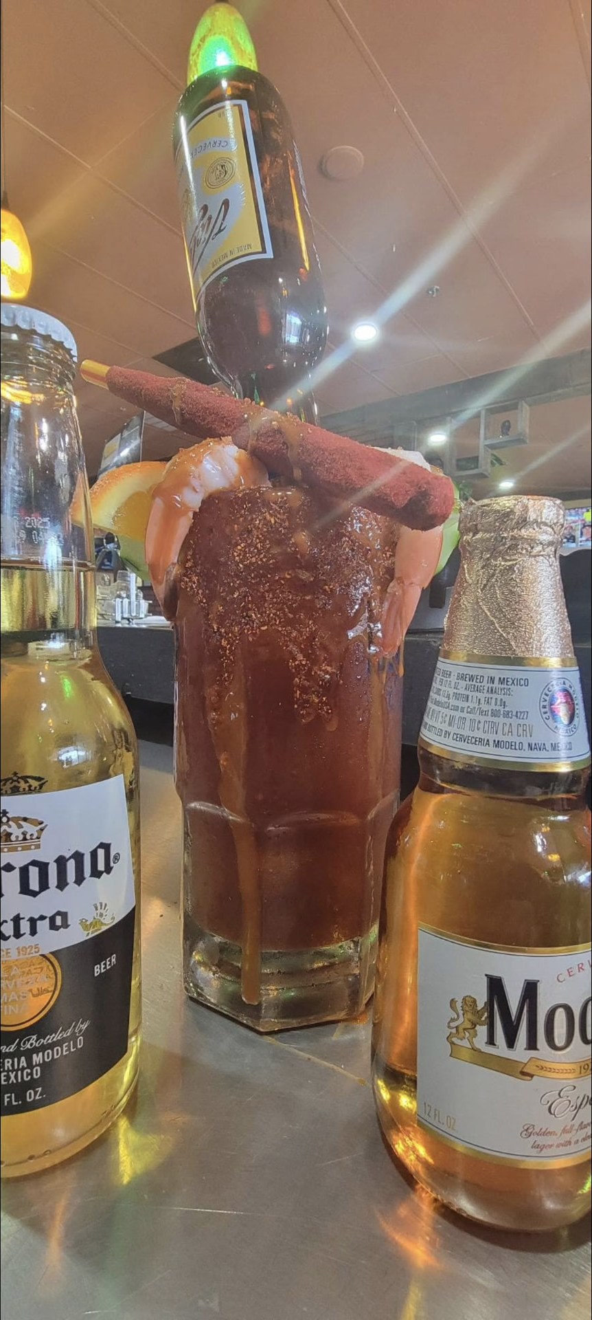Michelada with chamoy rim, shrimp and tamarind straw beside Mexican beers